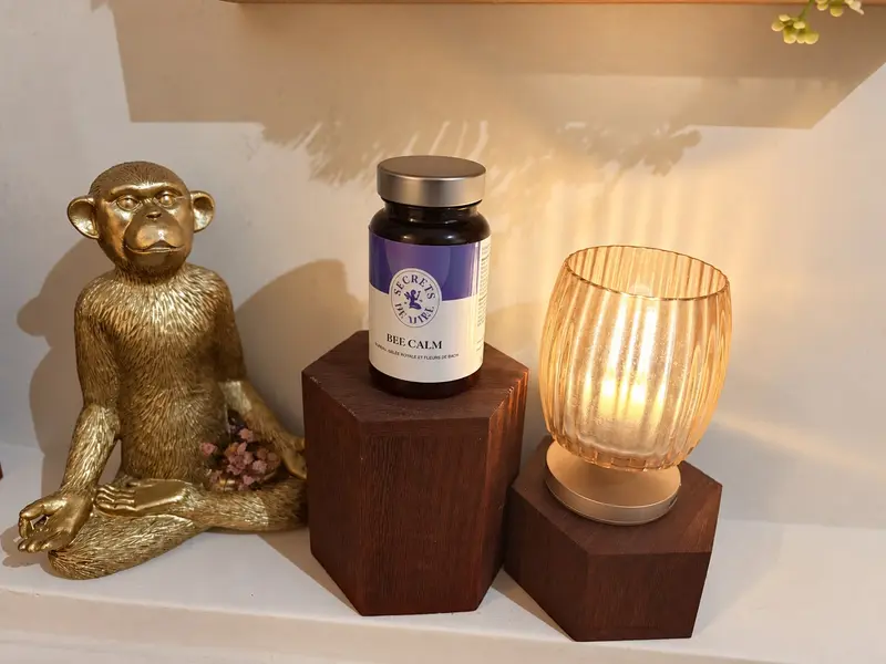 Flacon Bee Calm Secrets de Miel sur un socle en bois, à côté d’une lampe allumée